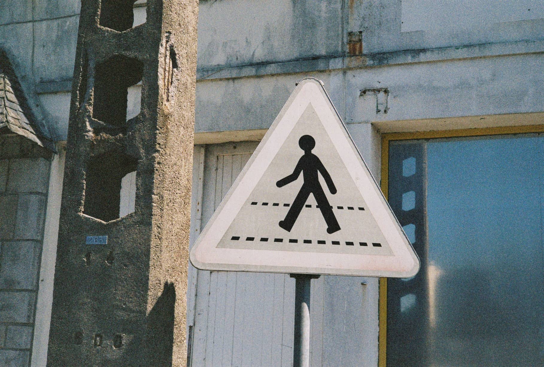 Dreieckiges Fußgängerschild vor einer verwitterten Hausfassade mit blau gerahmtem Fenster