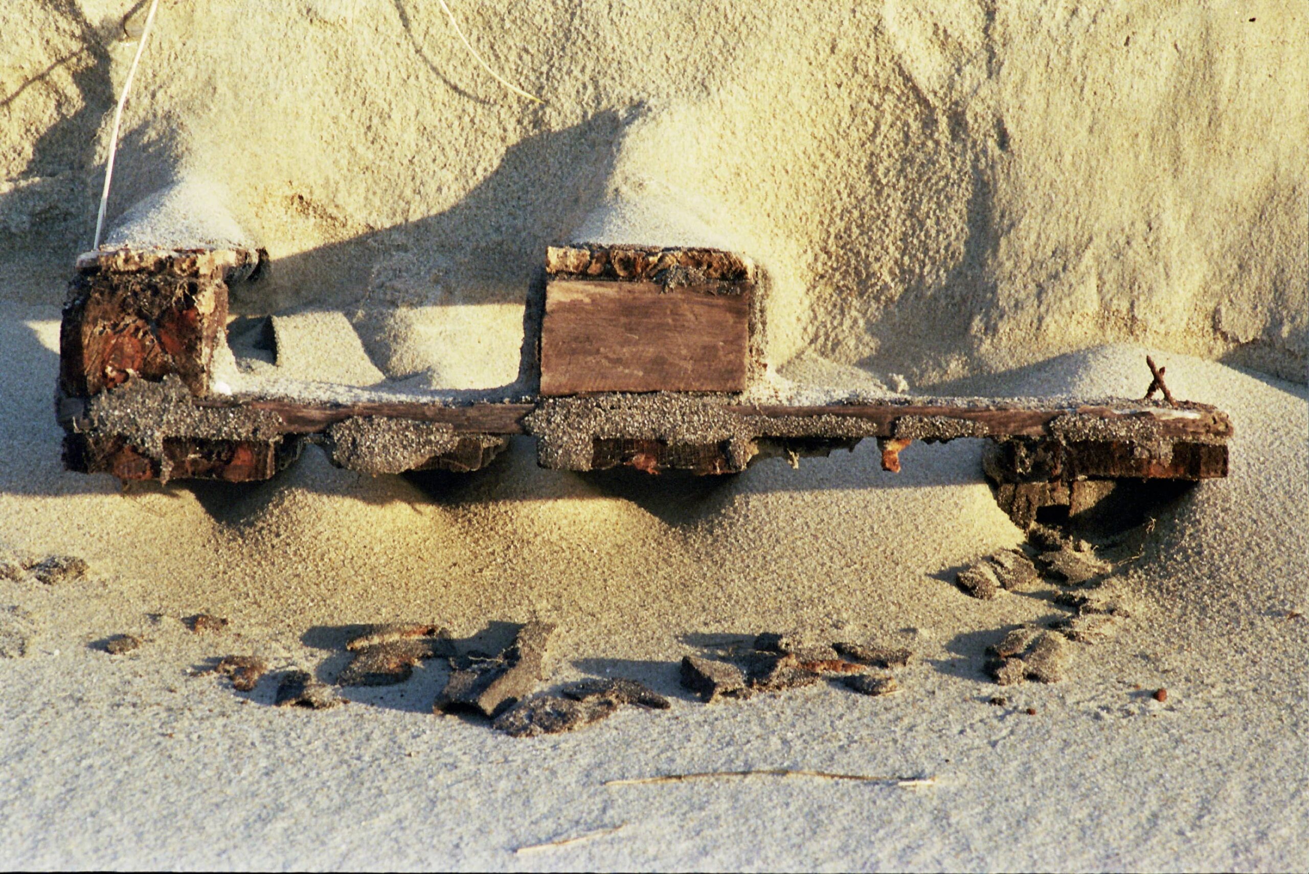 Verwittertes Holzstück, halb im Sand vergraben und mit Sand bestäubt