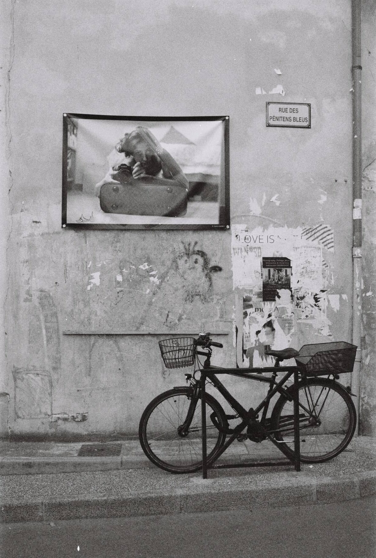 Zwei Fahrräder vor einer verwitterten Hauswand mit Fotoplakat und Straßenschild Rue des Pénitents Bleus, Schwarz-Weiß