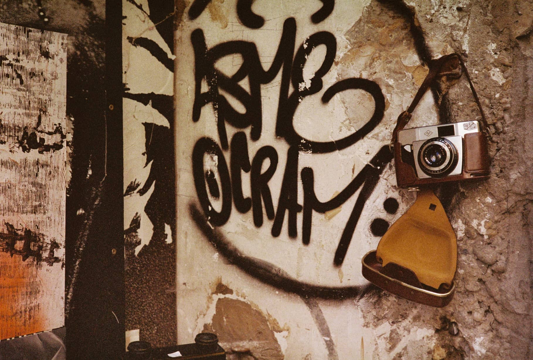 Alte Kamera mit geöffneter Ledertasche hängt an einer Wand mit Graffiti
