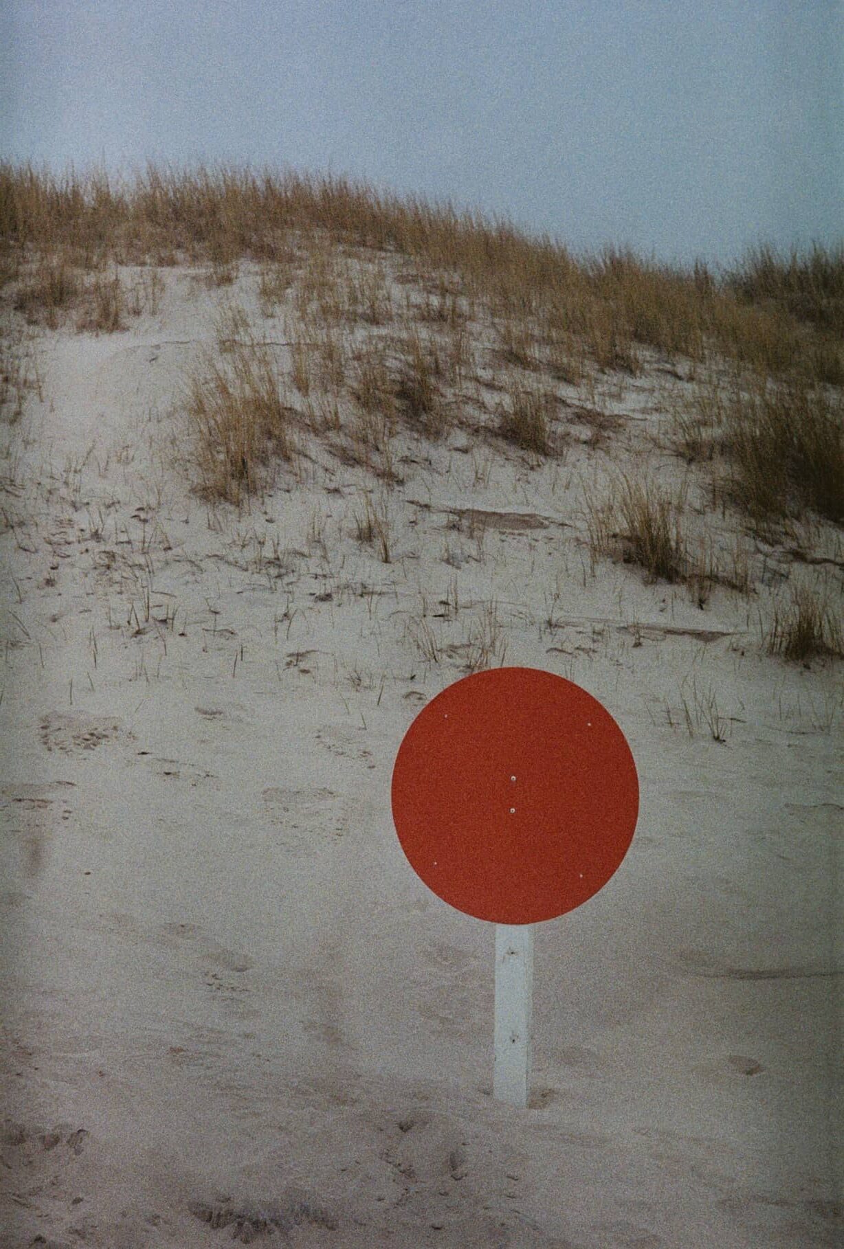Rote runde Scheibe auf einem Pfosten in einer Sanddüne mit Strandhafer