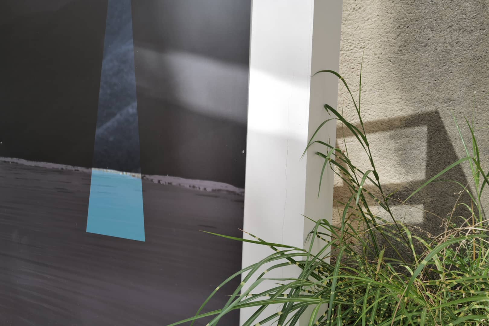 Plakat mit blauem Lichtstreifen über dunkler Landschaft, daneben Gras vor einer grauen Wand