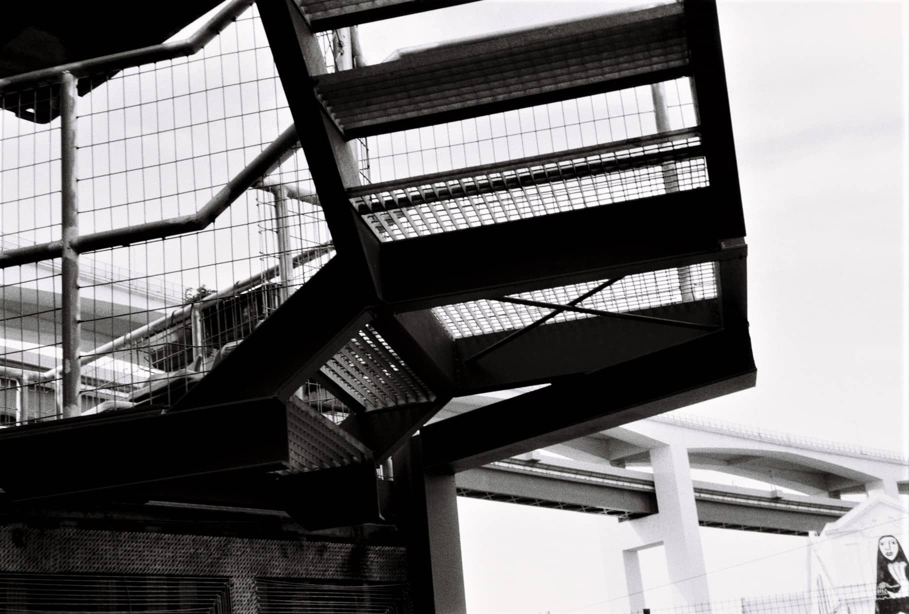 Metalltreppe mit Gitterstufen unter einer Autobahnbrücke, Schwarz-Weiß