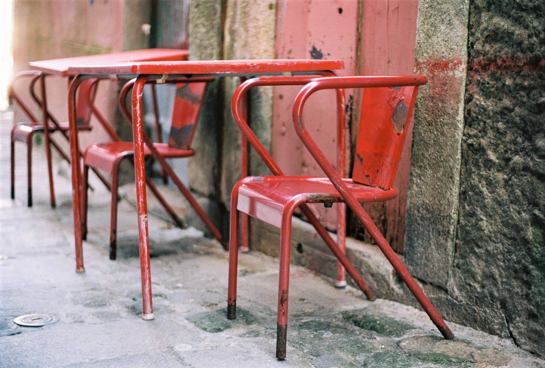 Rote Metallstühle und Tisch auf einem Gehweg vor einer roten Holzwand, Porto